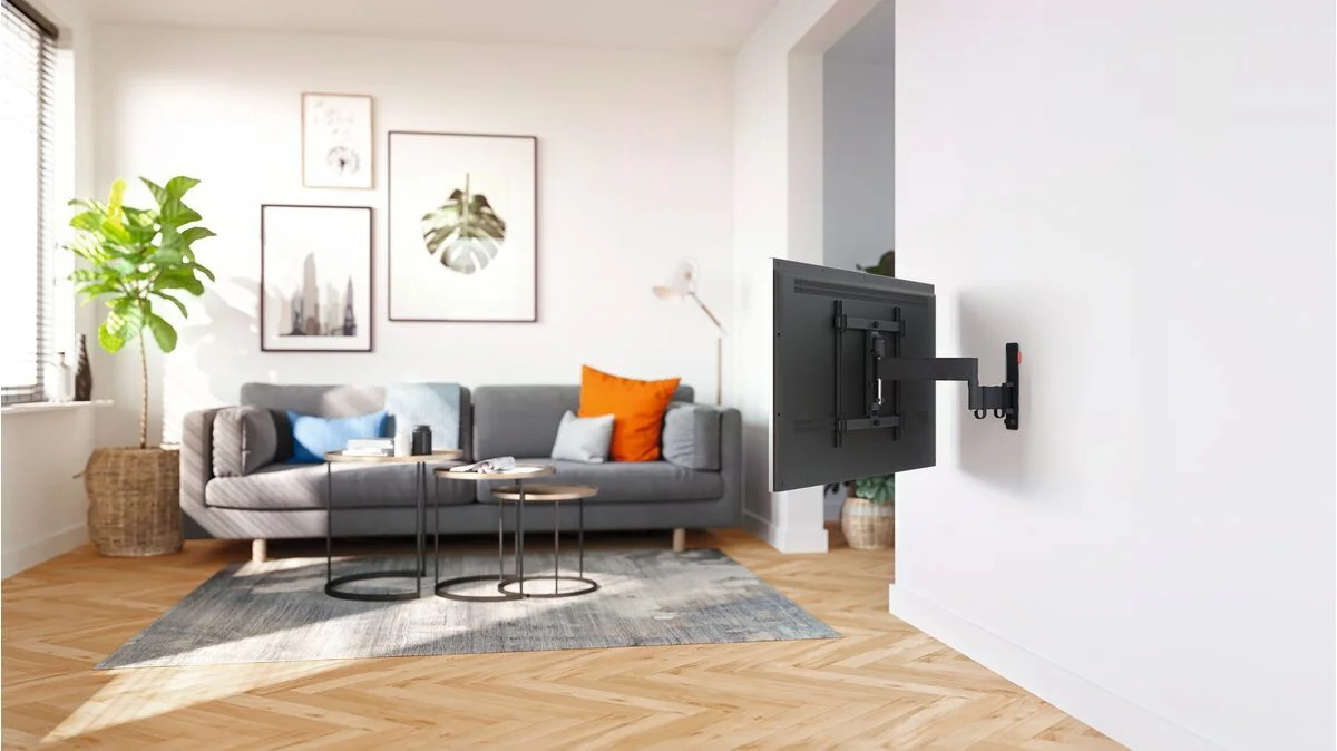 Wohnzimmer mit grauem Sofa, Couchtischen und einem an der Wand montierten TV.