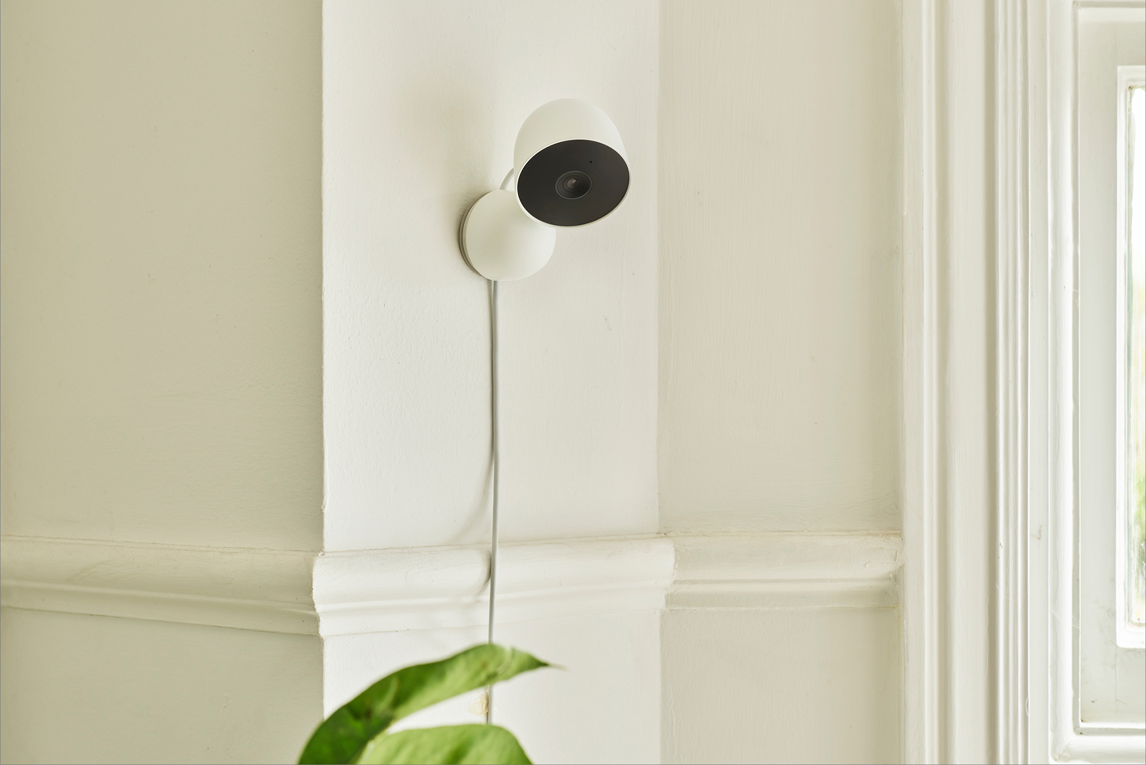 Een witte beveiligingscamera aan de muur, met een zwarte lens en een kabel.