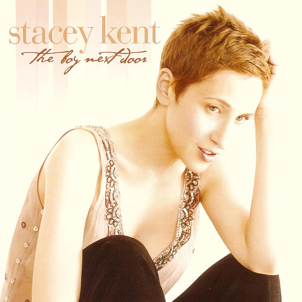 Stacey Kent album borítója. Fejét a kezére támasztja, a 'The Boy Next Door' címmel. Díszített felsőt és sötét nadrágot visel.