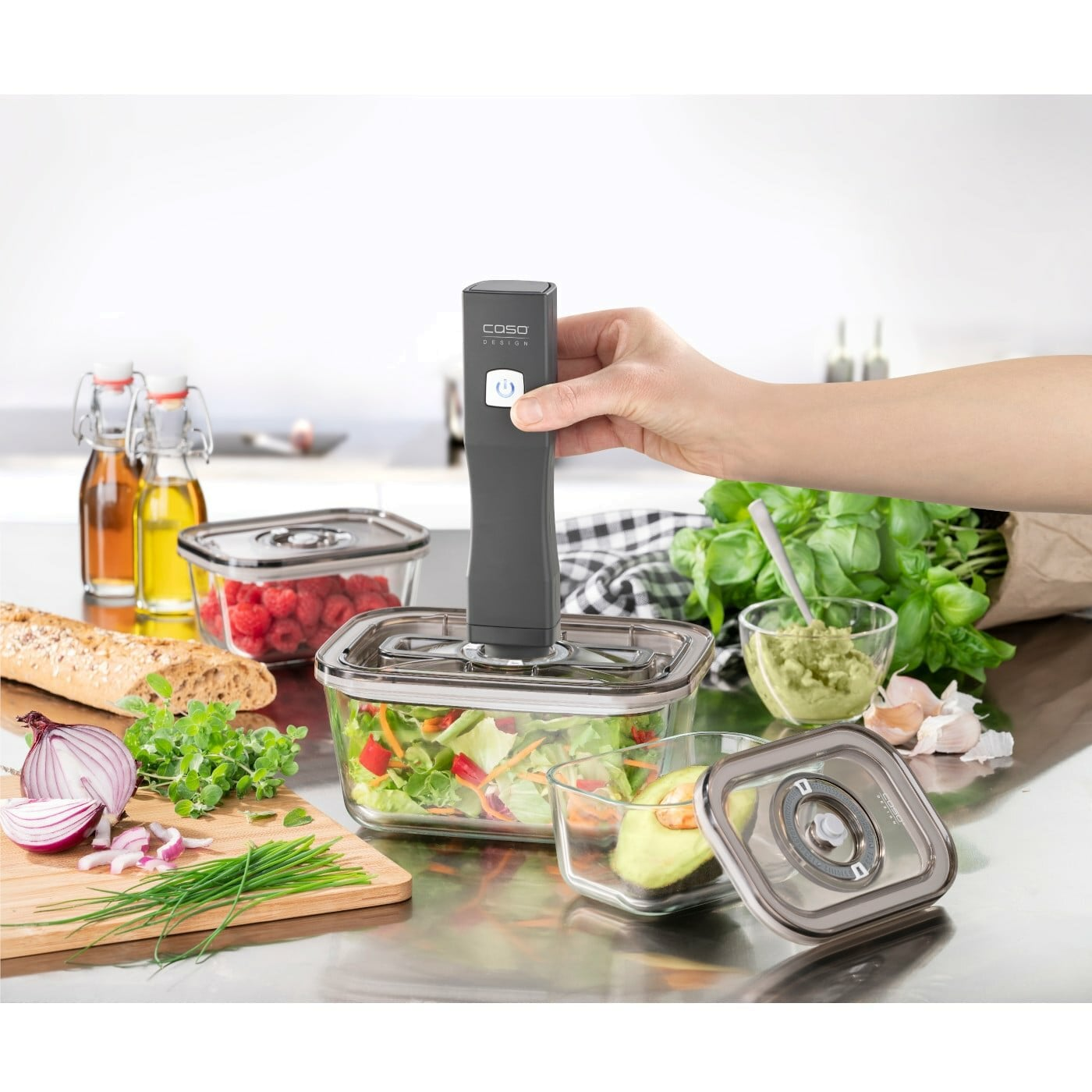 Eine Hand, die ein Vakuumiergerät auf einem Glasbehälter mit Salat verwendet.
