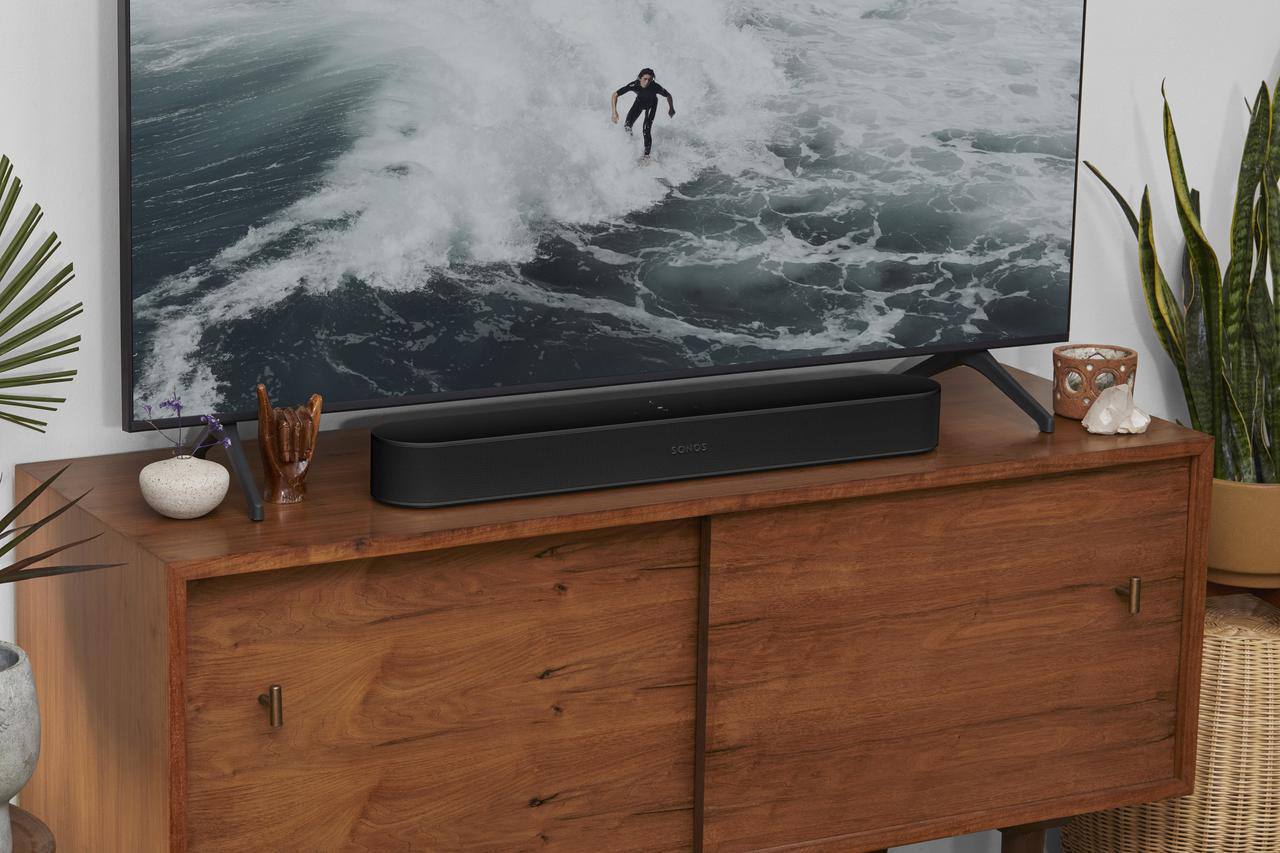 Schwarze Soundbar auf Holzschrank, TV zeigt Surfer auf Welle.