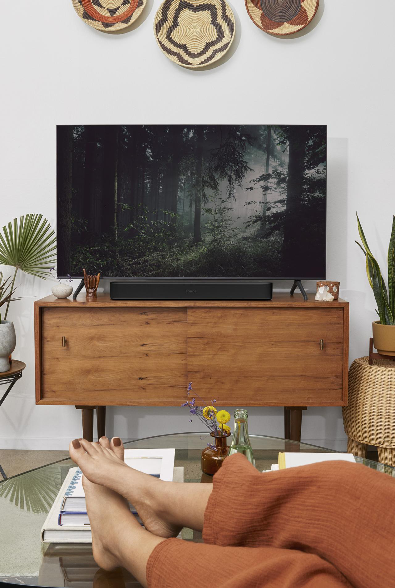 Wohnzimmer mit Fernseher auf Holzschrank, Pflanzen und Füßen einer Person.