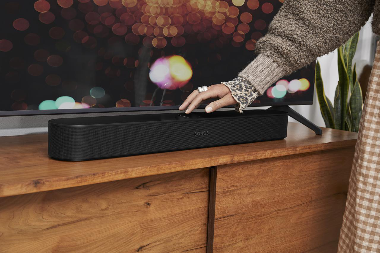 Hand berührt schwarze Soundbar auf Holzschrank, neben Fernseher.