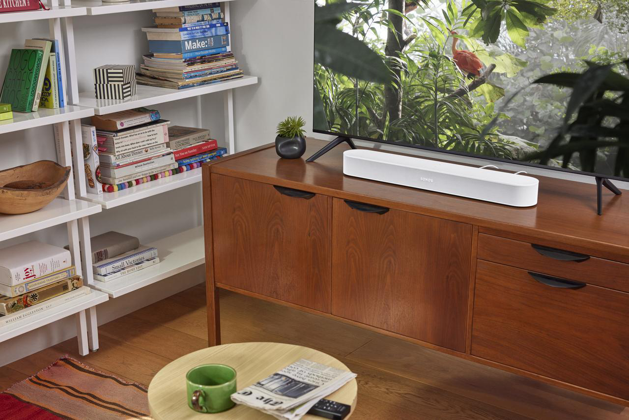 Ein Wohnzimmer mit einem Holzschrank, einer Soundbar oben, einem Fernseher, einem Bücherregal und einem Couchtisch.