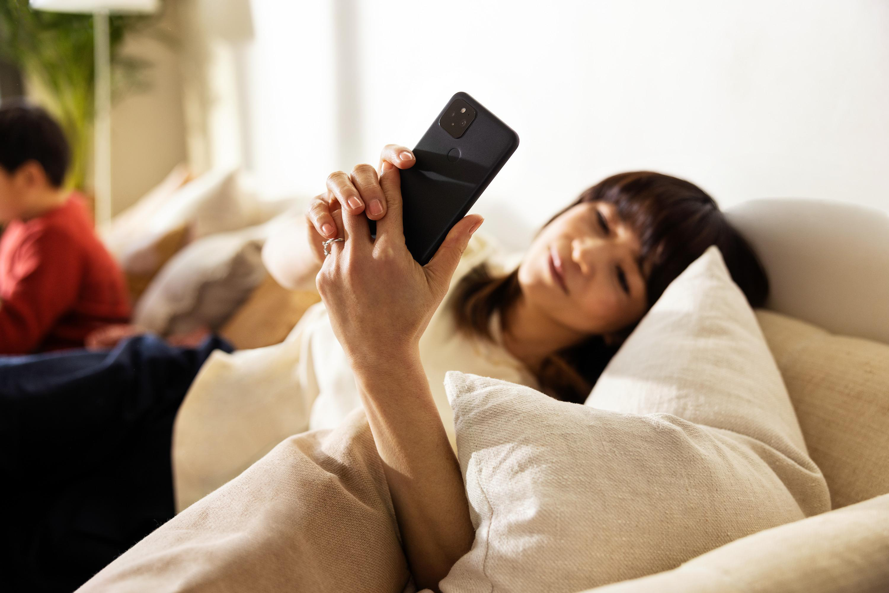Frau liegt auf Couch, hält Telefon, mit schwarzem Telefonhalter.