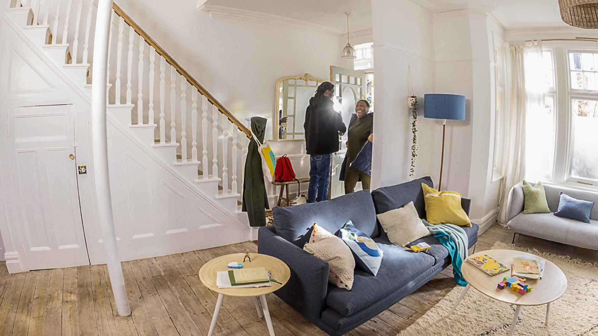 Wohnzimmer mit Couch, Couchtischen, Treppe und Personen im Flur.