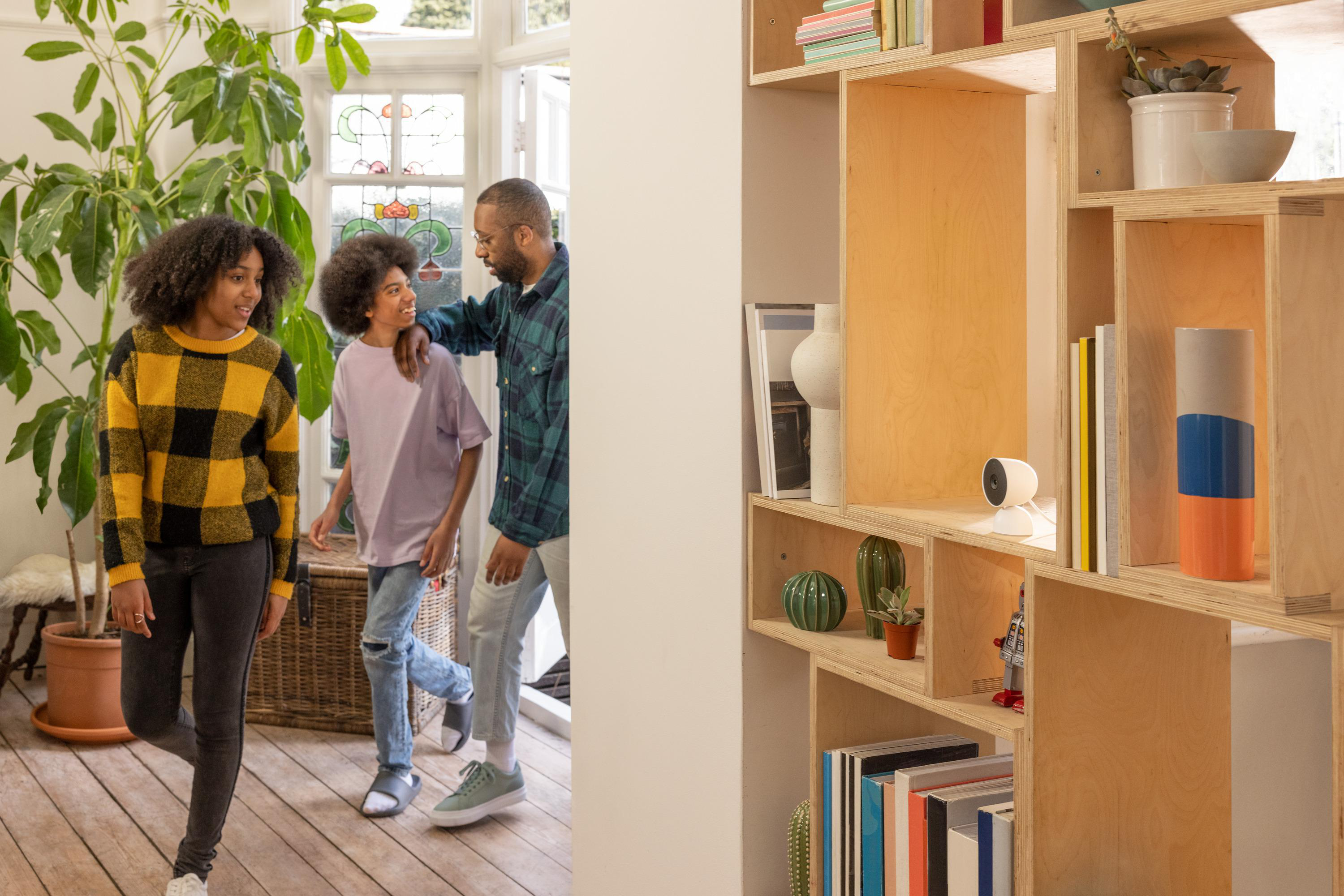 Eine Familie in einem Haus mit einem Bücherregal und einer intelligenten Kamera rechts.