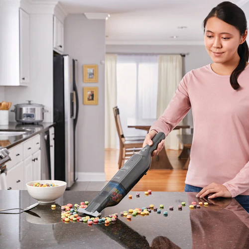 Une femme utilise un aspirateur à main pour nettoyer des bonbons colorés renversés sur un comptoir.