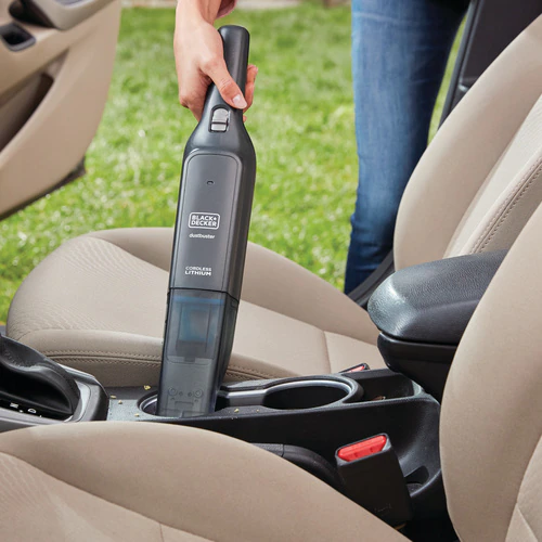 Une main tient un aspirateur noir et gris, aspirant un siège de voiture.