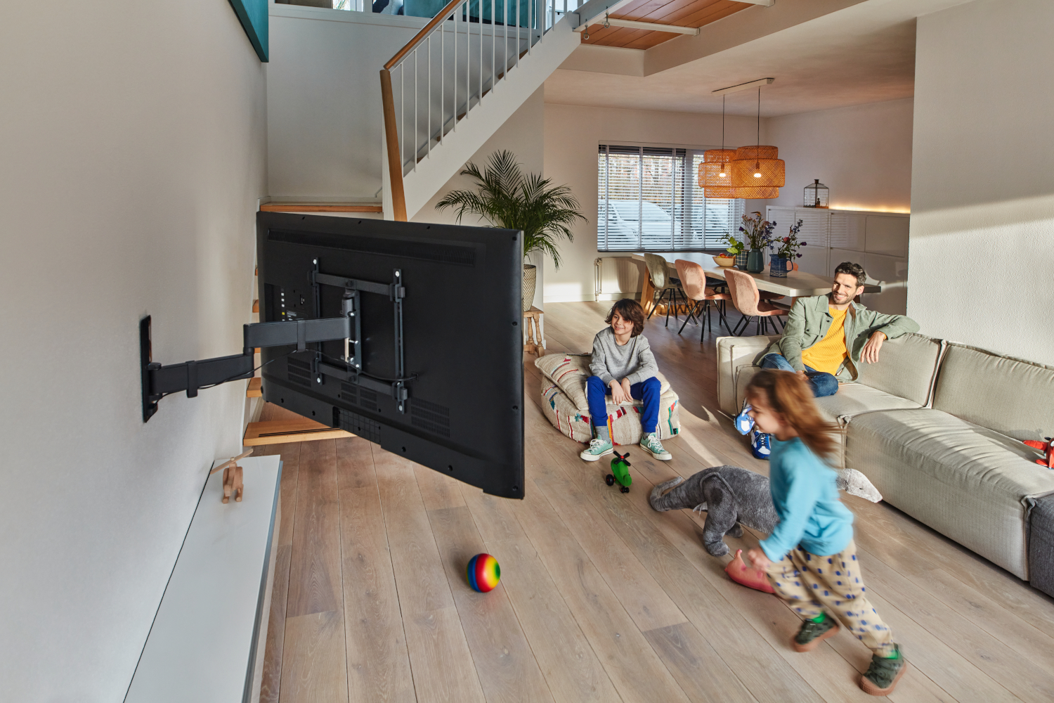 Woonkamer met een tv aan de muur. Een gezin is in de kamer met een kind dat speelt.