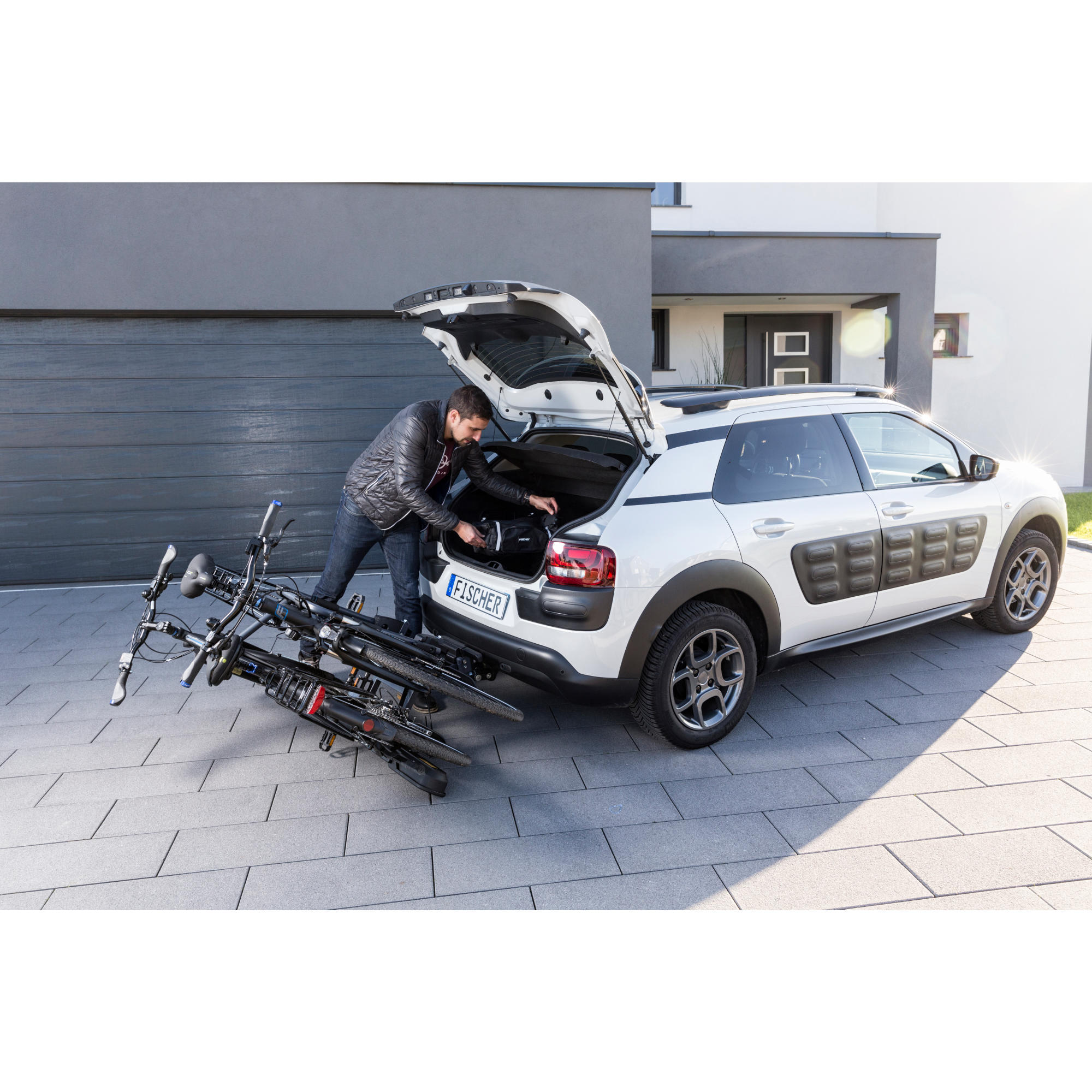 Ein weißes Auto mit Fahrrädern auf einem Träger. Eine Person lädt die Fahrräder ins Auto.