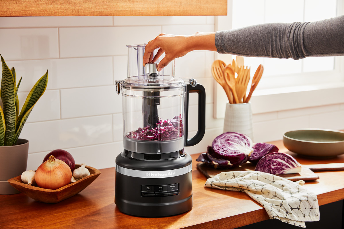 Die Hand einer Person, die einen Foodprozessor mit Rotkohl auf einer Holzoberfläche benutzt.
