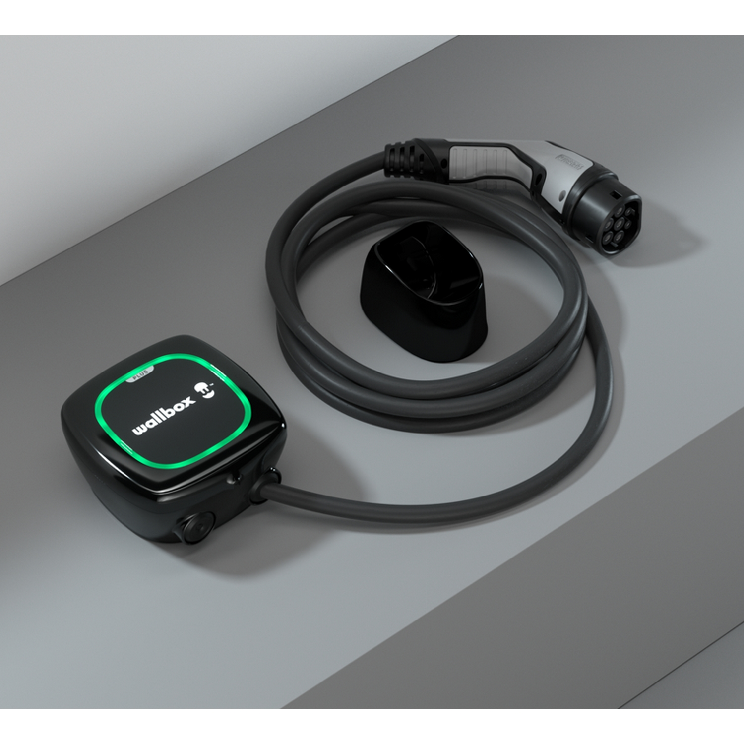 Un cargador de vehículo eléctrico Wallbox negro con luz verde, cable y conector sobre una superficie gris.