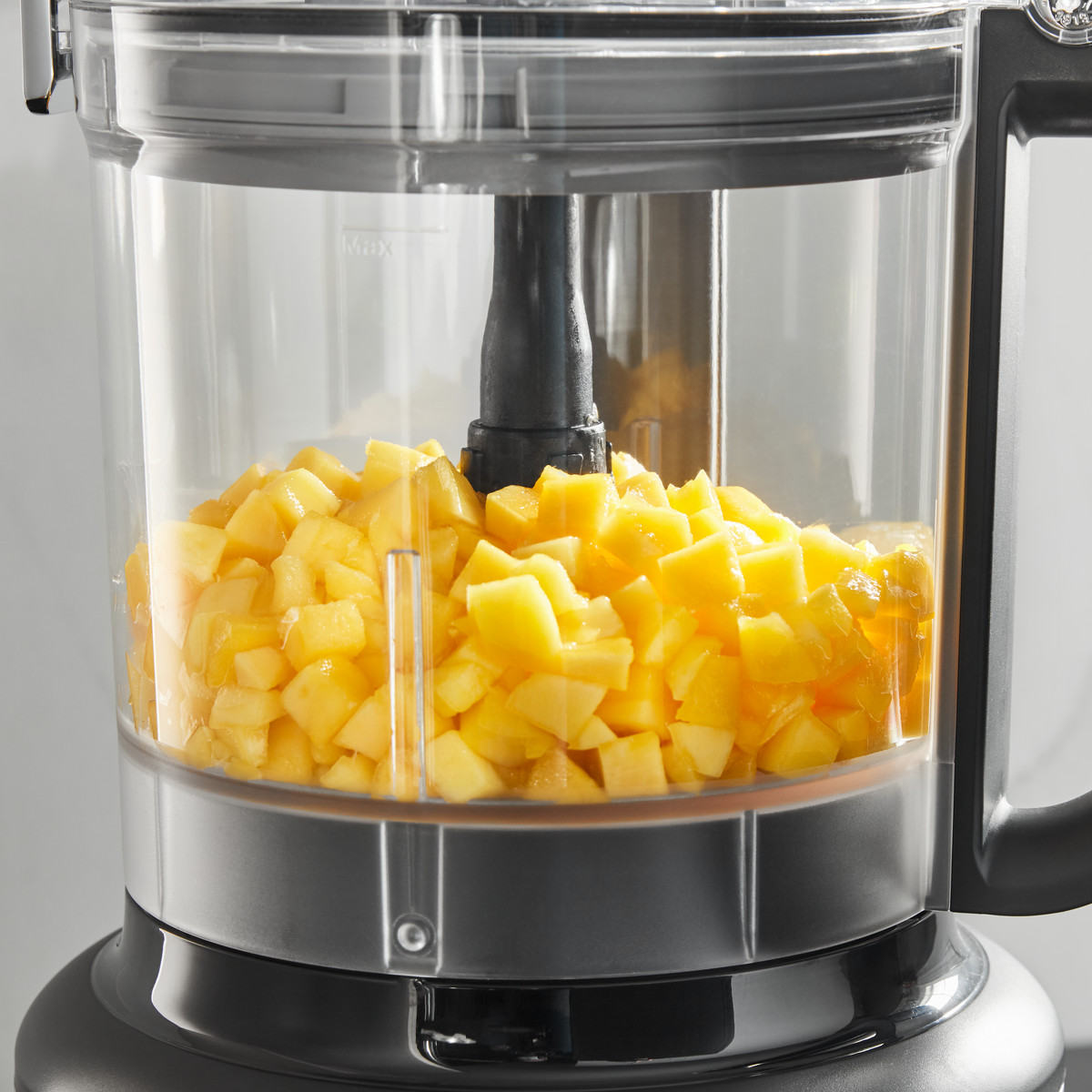 Küchenmaschine mit gewürfeltem gelben Obst in der Schüssel.