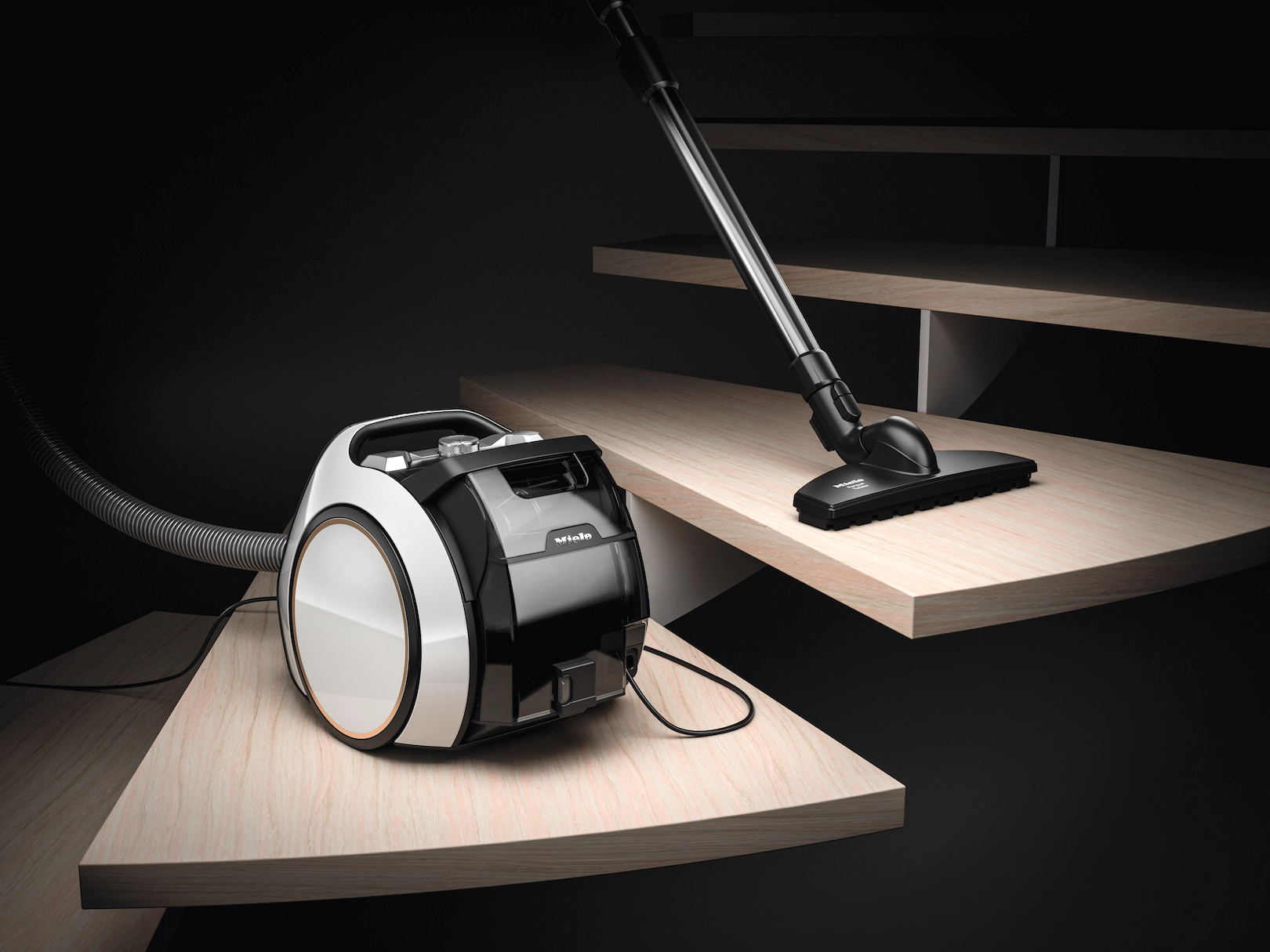Aspirateur noir et blanc sur escalier en bois. La buse est sur la marche.
