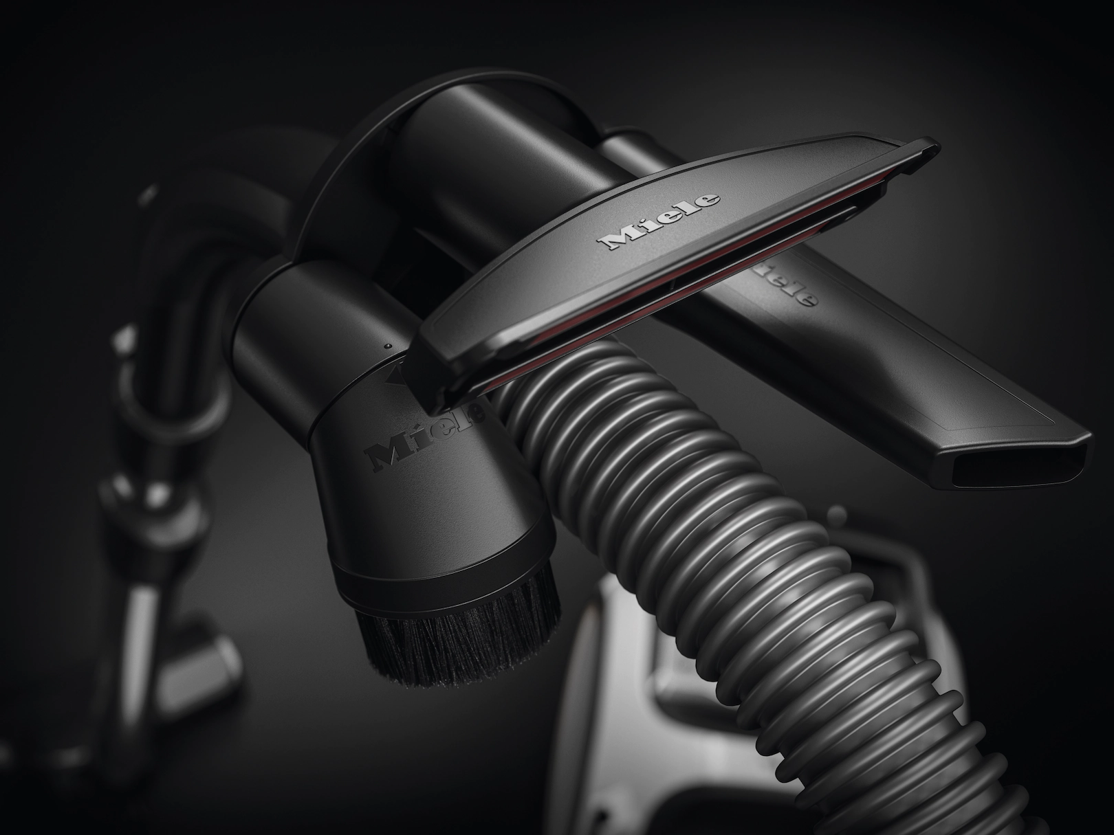 Gros plan d'accessoires d'aspirateur noirs, dont une brosse et un tuyau, sur une surface noire.