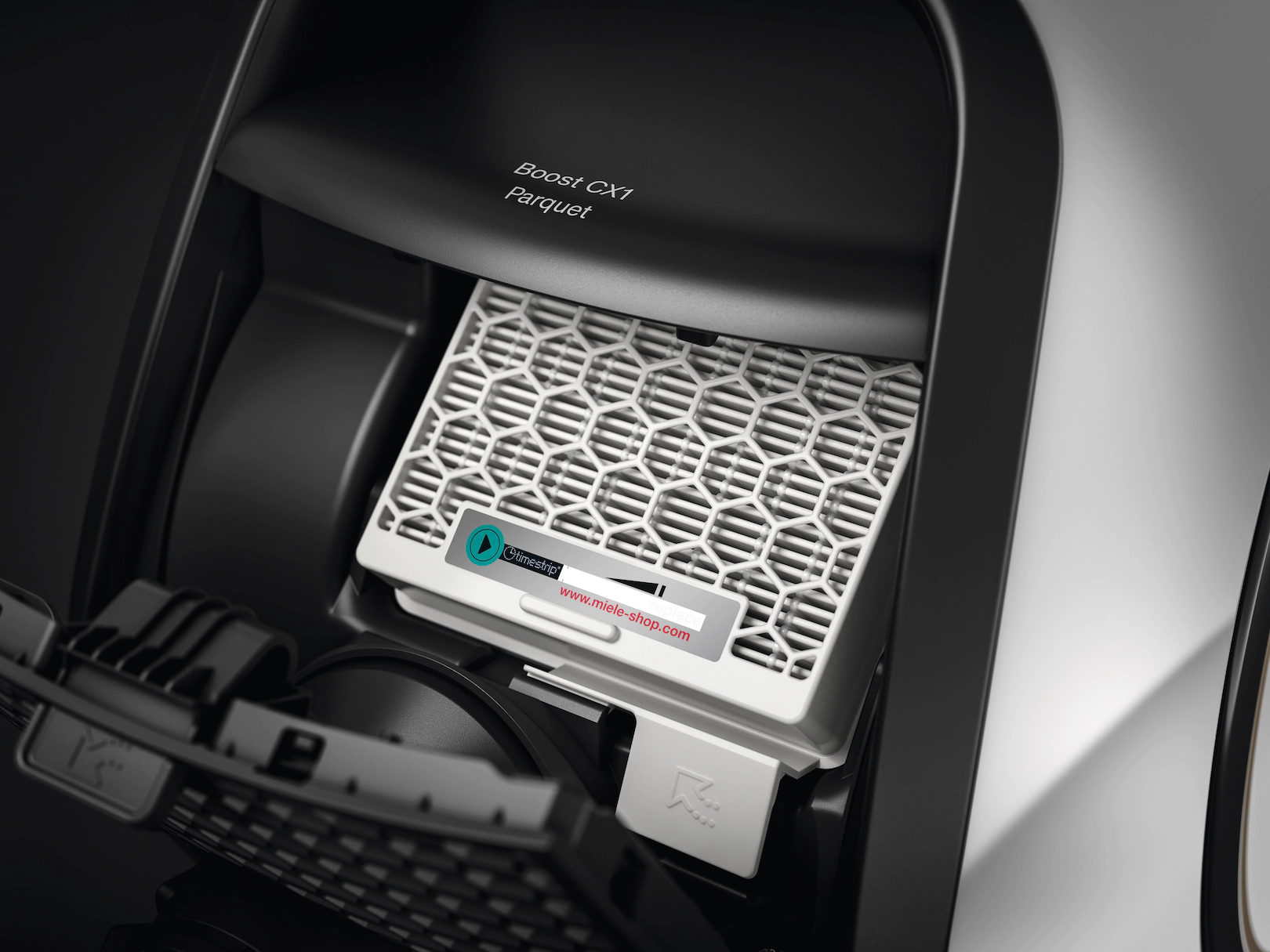 Compartiment du filtre d'aspirateur ouvert. Filtre blanc avec cadre noir. Texte : 'Boost CX1 Parquet'.