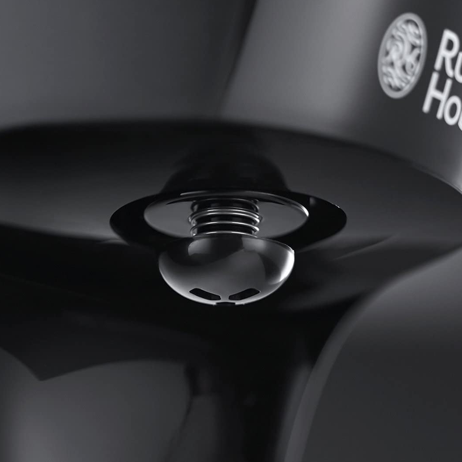 Primo piano di un componente nero di un elettrodomestico. Una bobina argentata, un pezzo nero curvo con fori e il logo Russell Hobbs sono visibili.