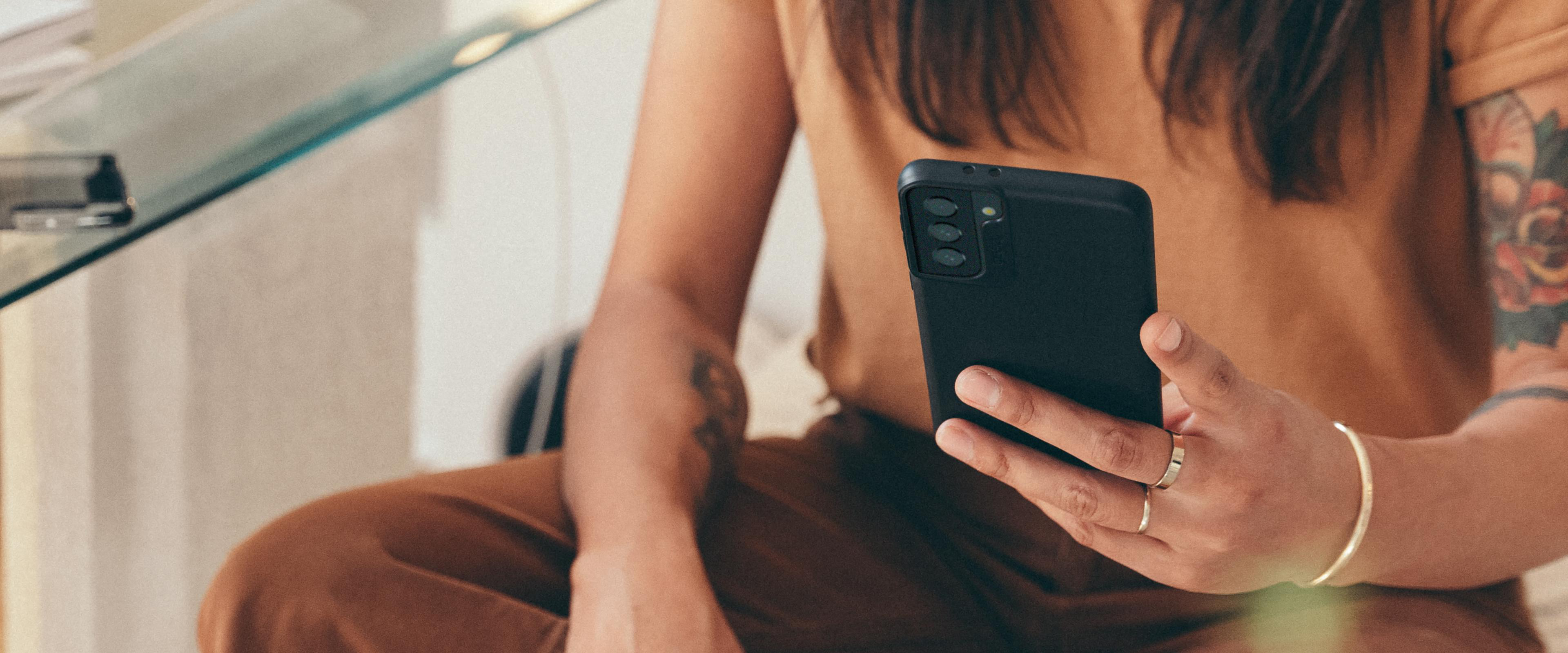 Eine Person hält ein schwarzes Smartphone mit drei Rückkameras. Die Person trägt ein braunes Oberteil.