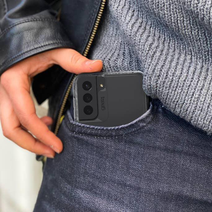 Eine Person steckt ein Telefon in ihre Tasche. Das Telefon befindet sich in einer durchsichtigen Hülle. Die Tasche ist an Jeans.