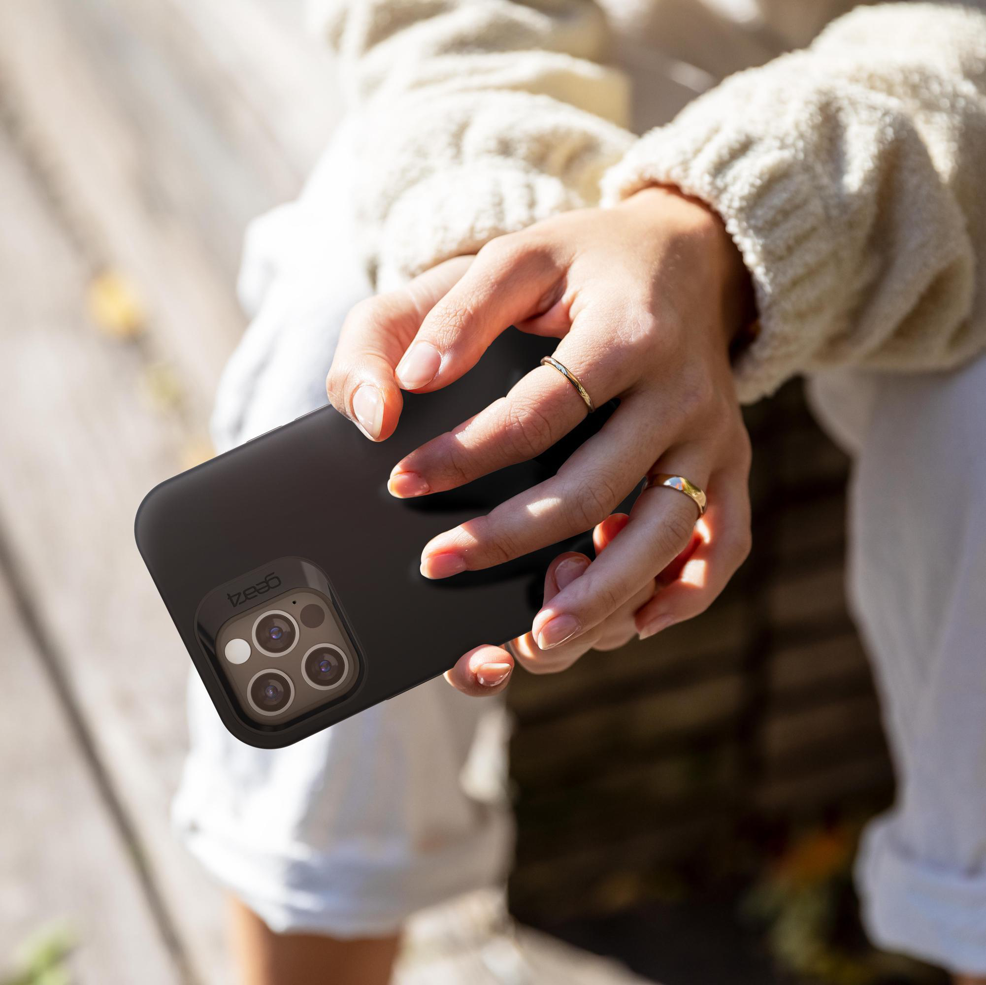 Person hält ein schwarzes Telefon mit Hülle, goldener Ring und verschwommener Hintergrund.