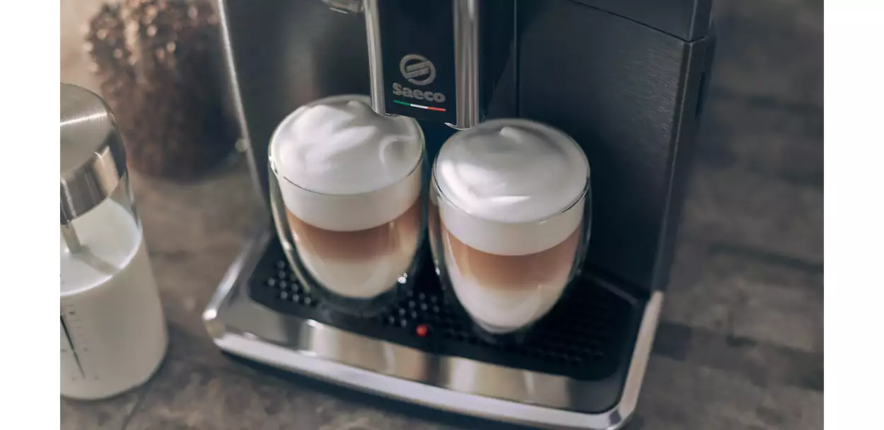 Two glasses of latte macchiato on a coffee machine. Frothy milk on top. Blurry background.