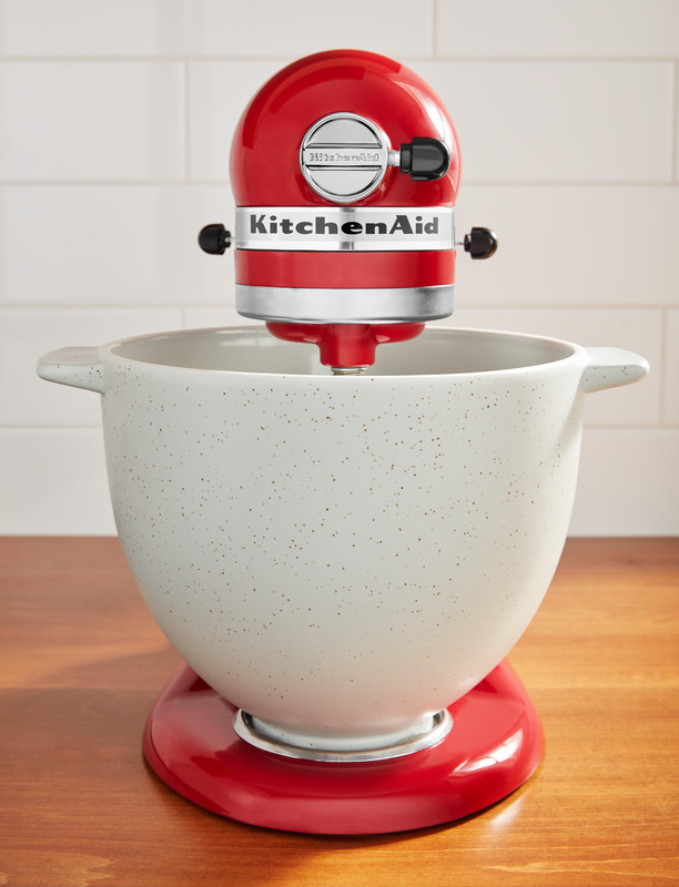 Roter KitchenAid-Mixer mit weißer Schüssel, auf Holzoberfläche, vor weißer Kachelwand.