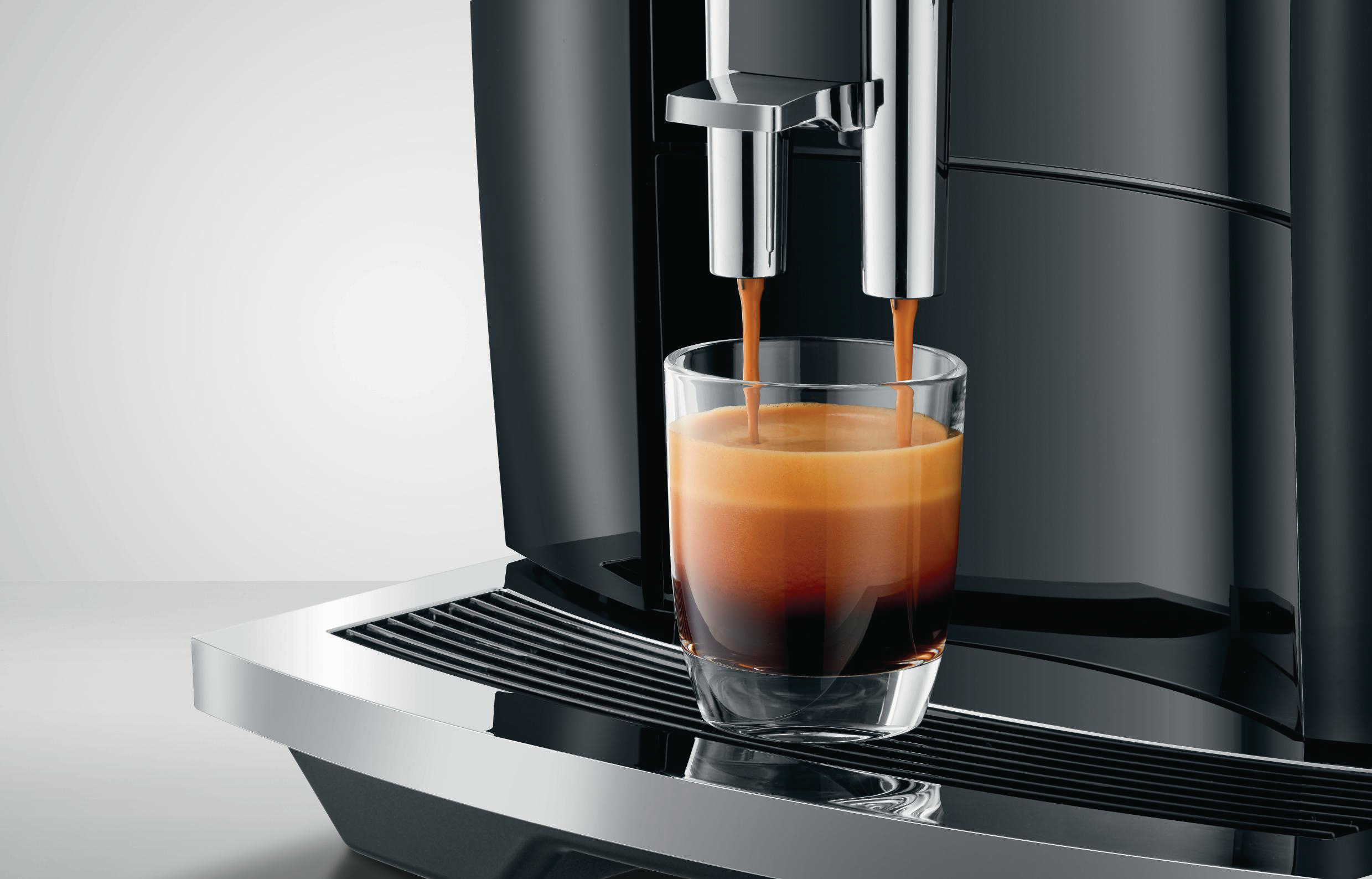 Espressomaschine gießt Kaffee in ein Glas. Dunkler Kaffee, glänzende Maschine, weißer Hintergrund.