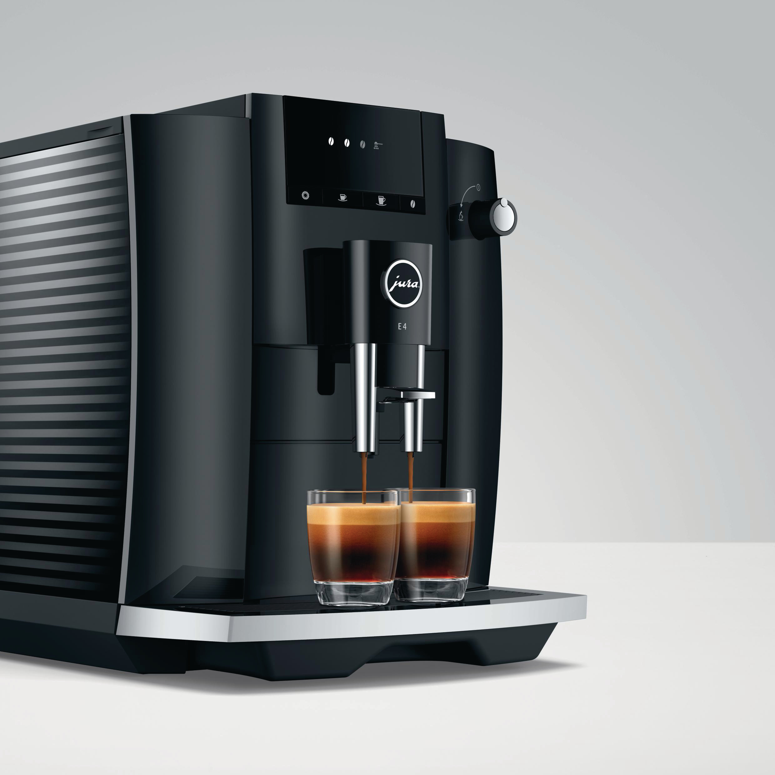 Eine schwarze Jura E4 Espressomaschine, mit zwei Gläsern, die mit Kaffee gefüllt werden, auf weißem Hintergrund.