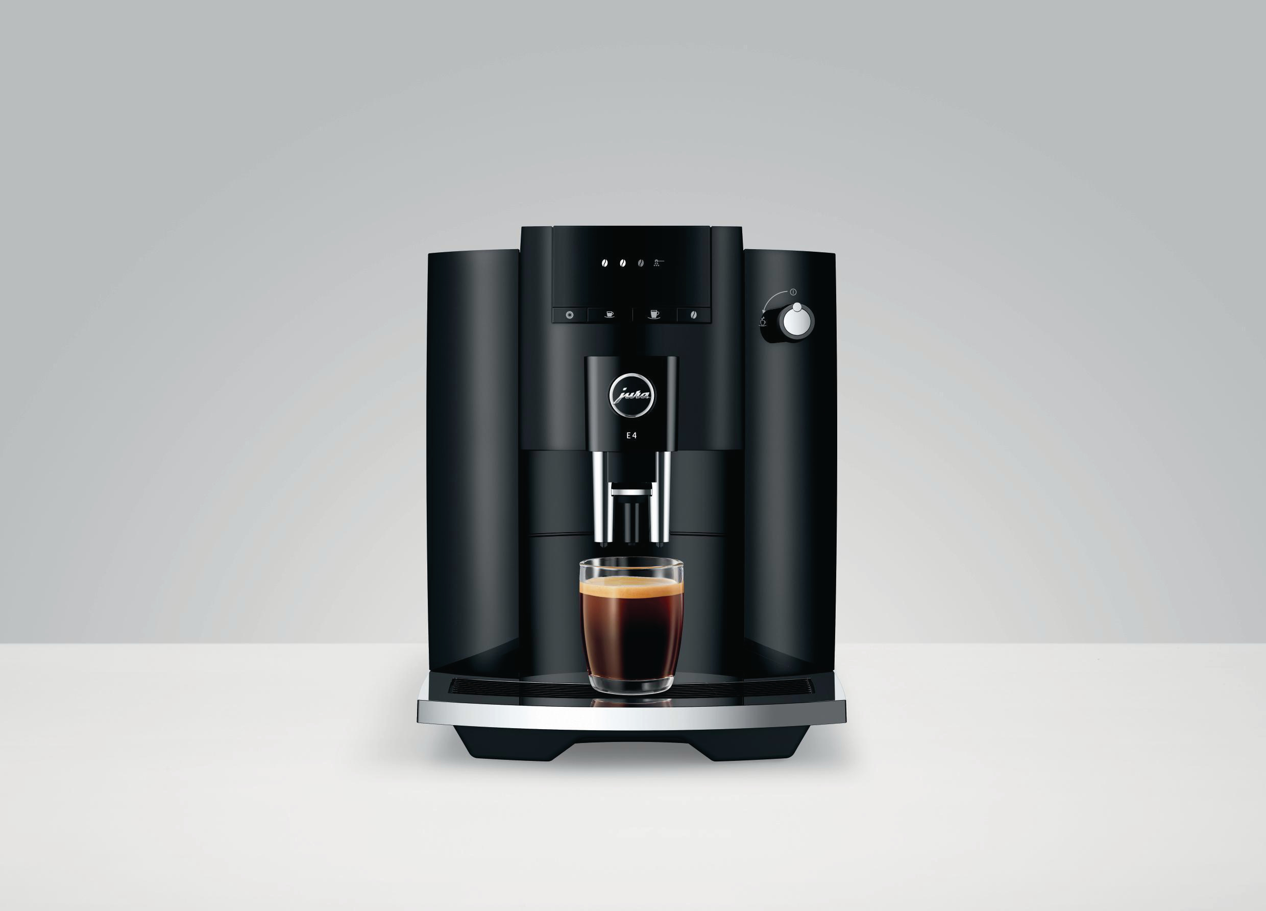 Eine schwarze Jura Kaffeemaschine mit einem Glas Espresso. Sie steht auf einer weißen Oberfläche.