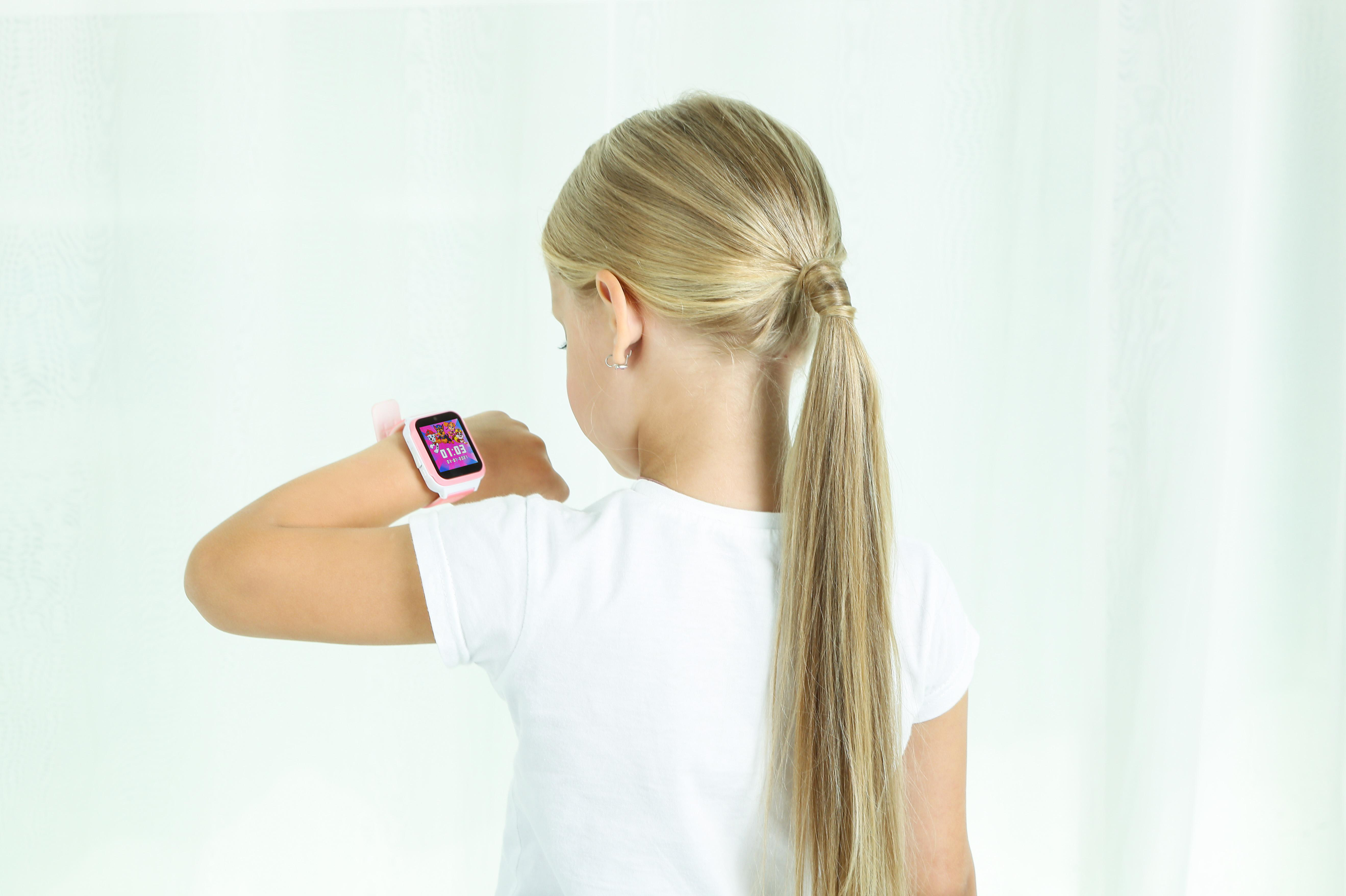 Ein Mädchen betrachtet ihre pinke Smartwatch, Rückansicht.