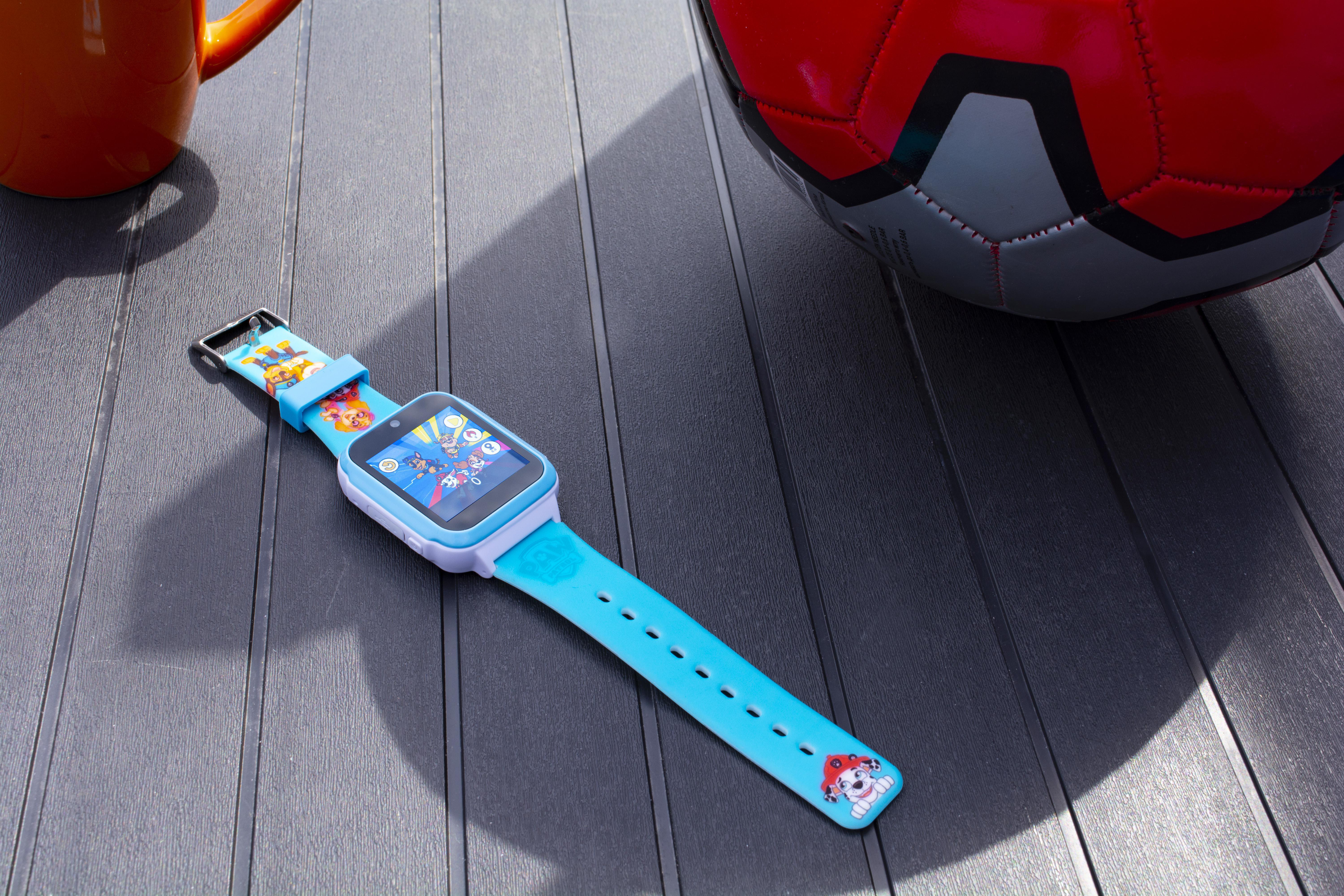 Eine Kinder-Smartwatch mit Paw Patrol-Charakteren. Die Uhr liegt auf einer dunklen Oberfläche, neben einem Ball.