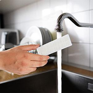 Hand hält einen weißen Filter unter fließendem Wasser aus einem Wasserhahn.