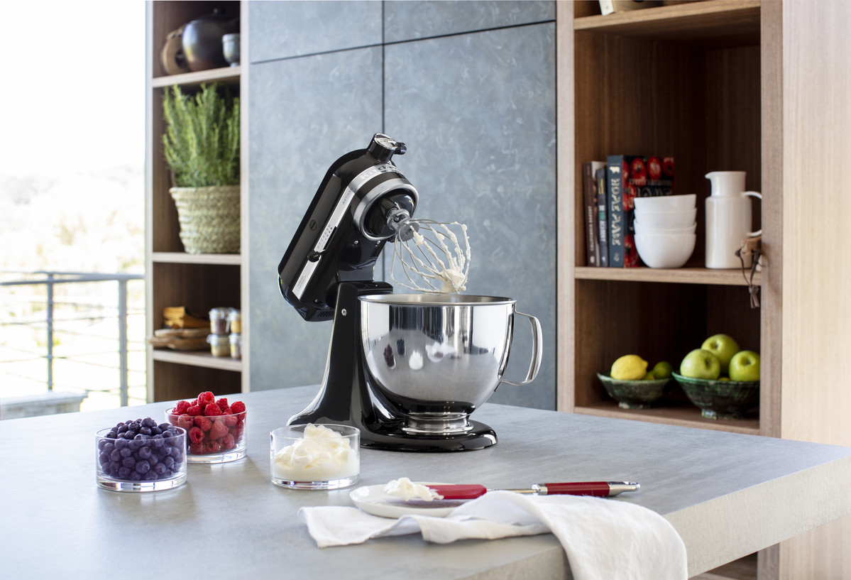 Ein schwarzer KitchenAid-Mixer mit Edelstahlschüssel steht auf einer Arbeitsplatte.