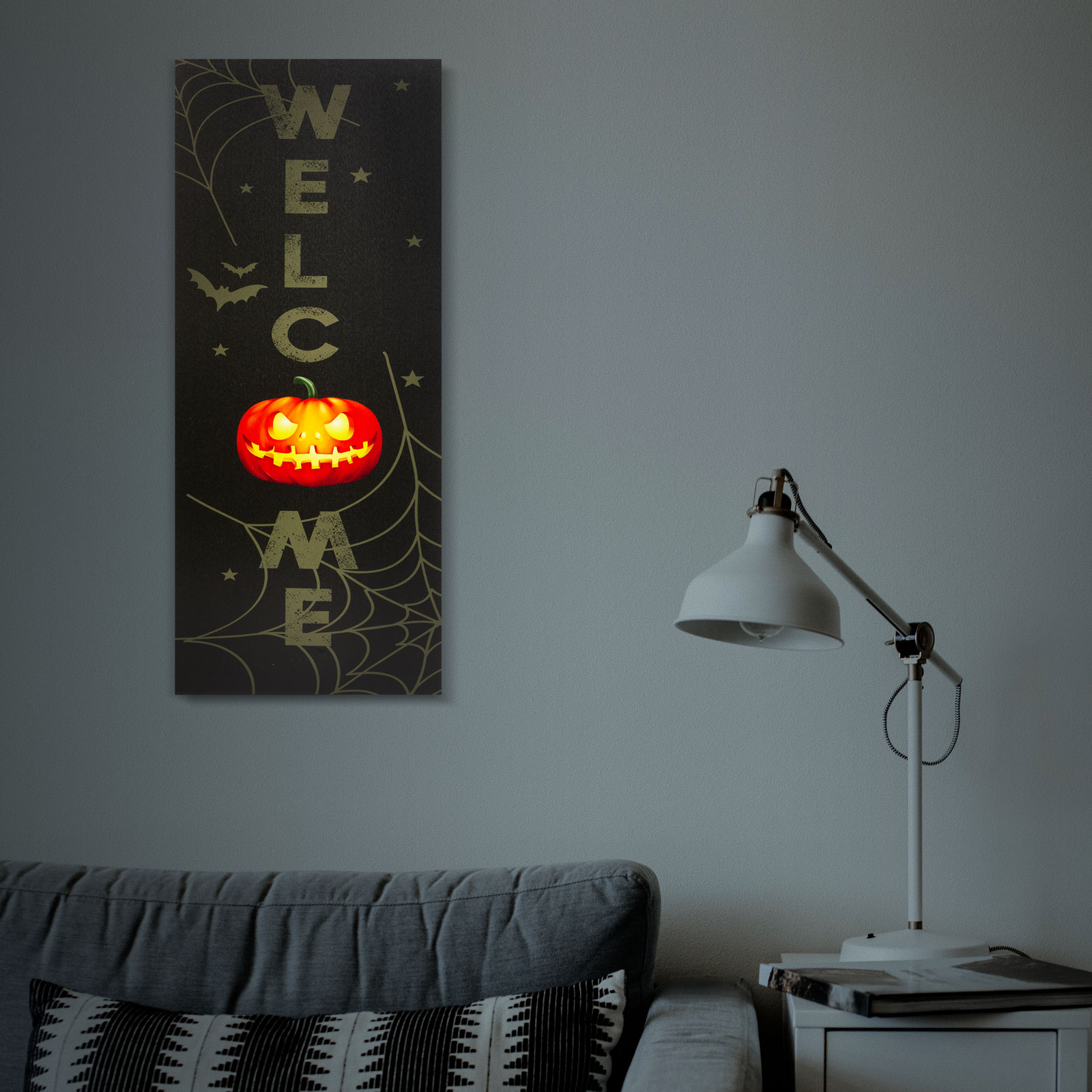 Halloween témájú üdvözlőtábla tökkel és pókháló mintával, amelyet egy lámpa világít meg.