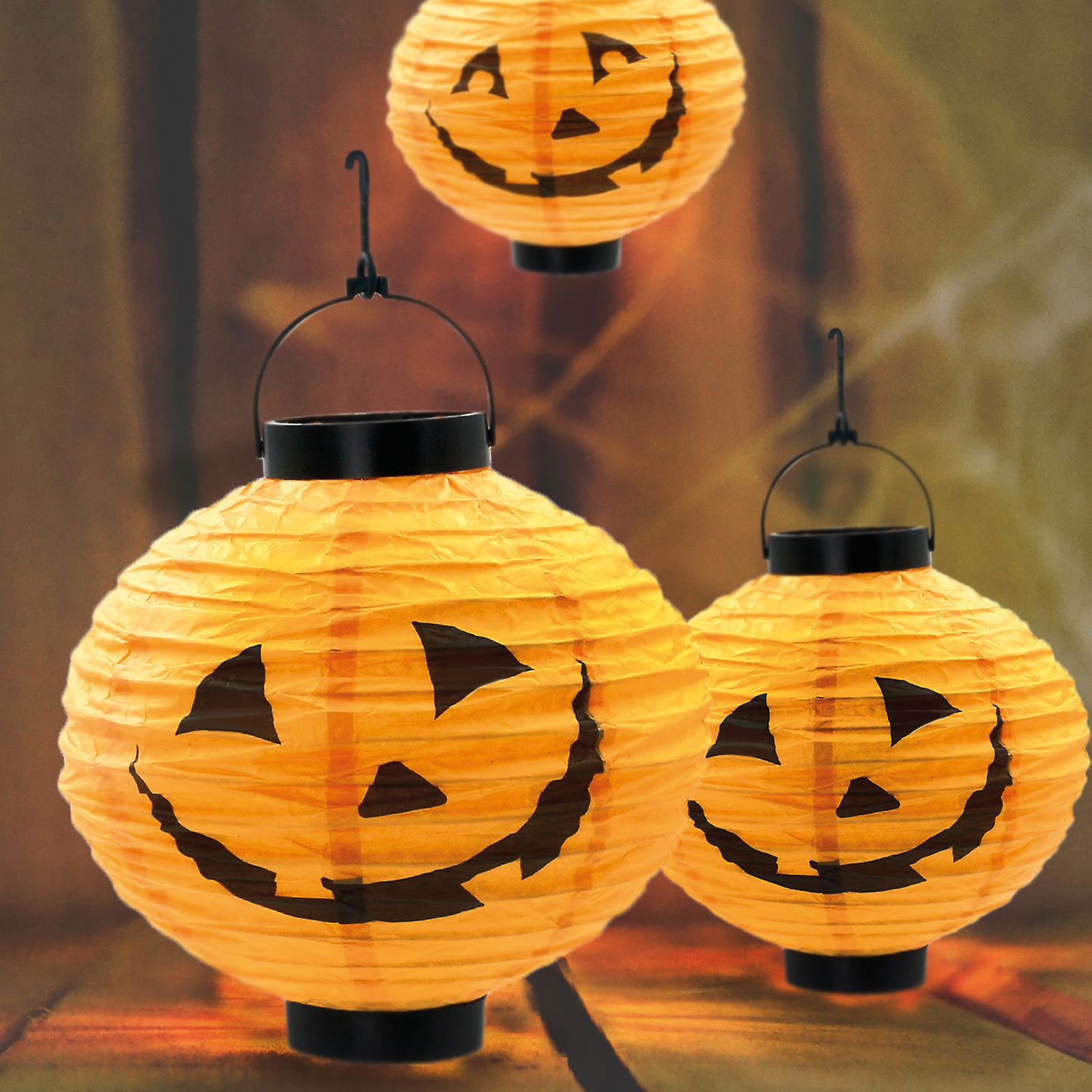 Papír töklámpások faragott arcokkal, felülről lógnak, sötét háttér.