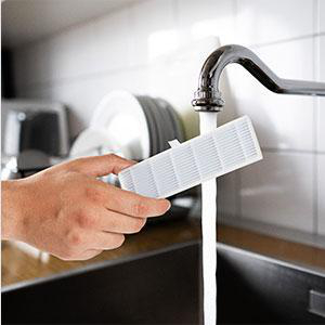 Ein weißer Filter wird unter fließendem Wasser gewaschen. Das Wasser ist klar, der Filter weiß.