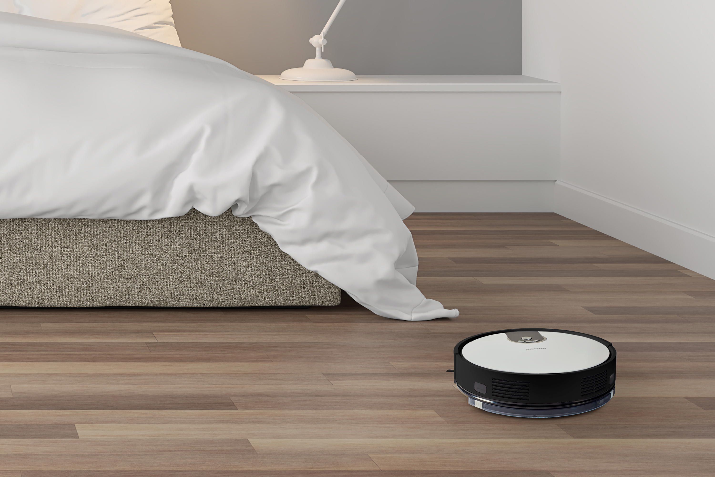 Roboter-Staubsauger auf Hartholzboden in der Nähe eines Betts.