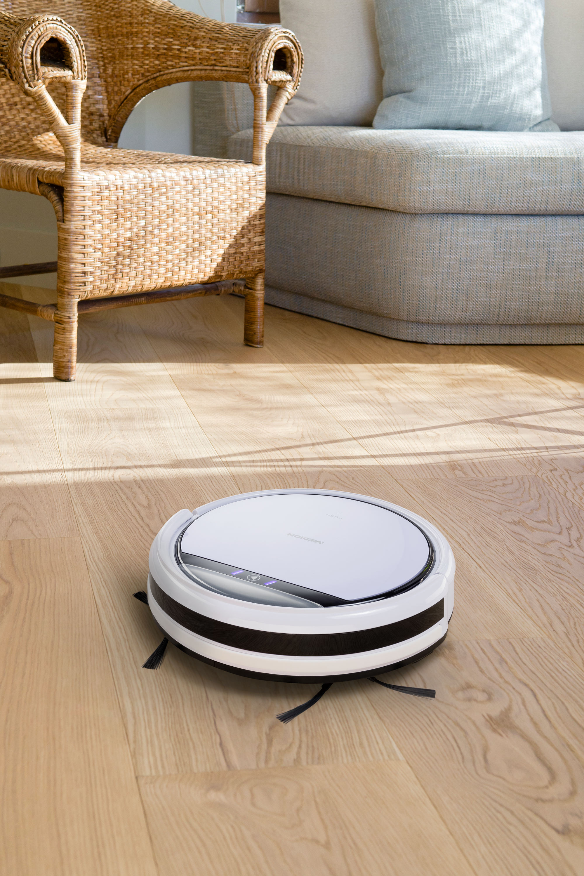 Ein weißer Roboter-Staubsauger, der einen Holzboden reinigt.