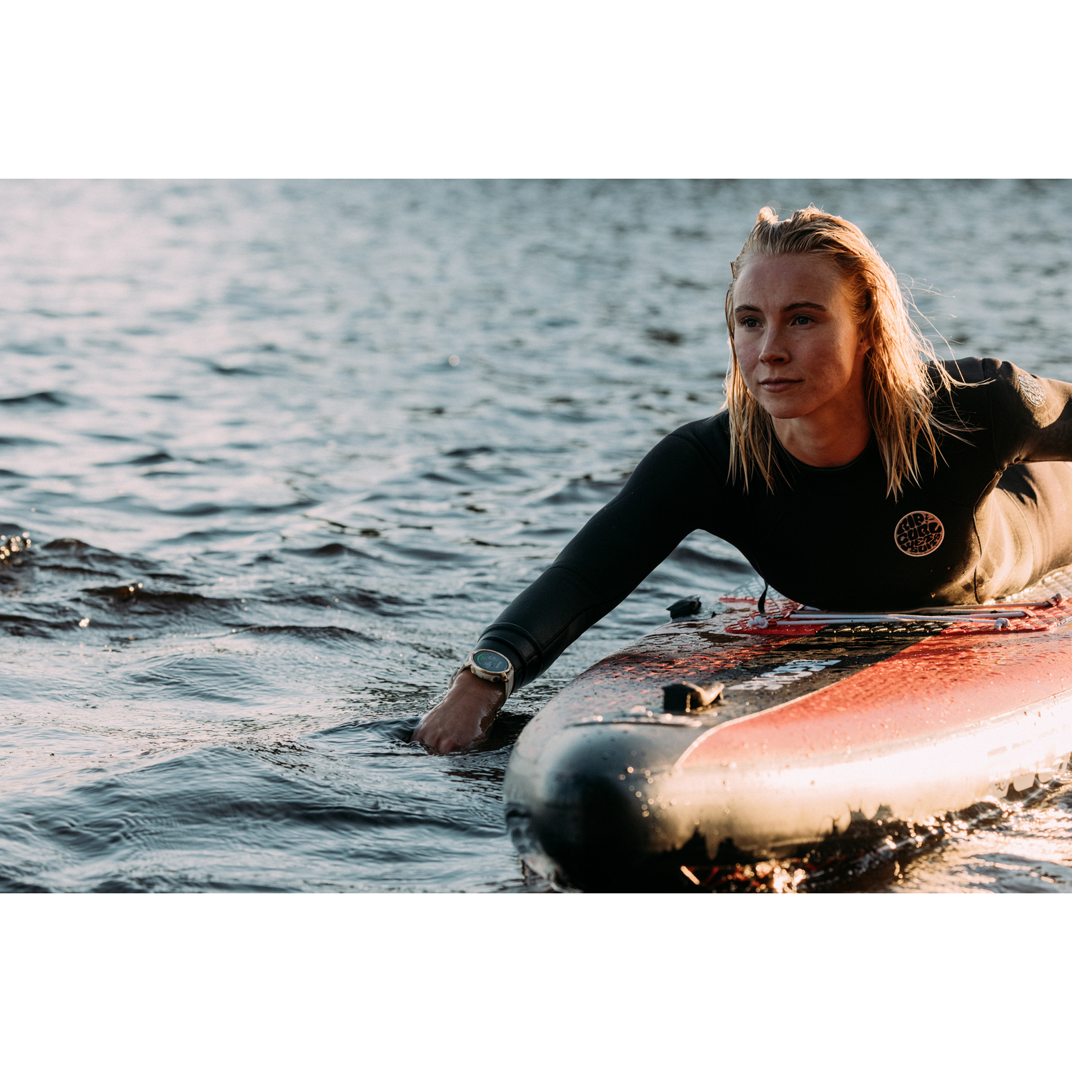 Mujer en una tabla de surf en el agua. El sol se refleja en el agua.