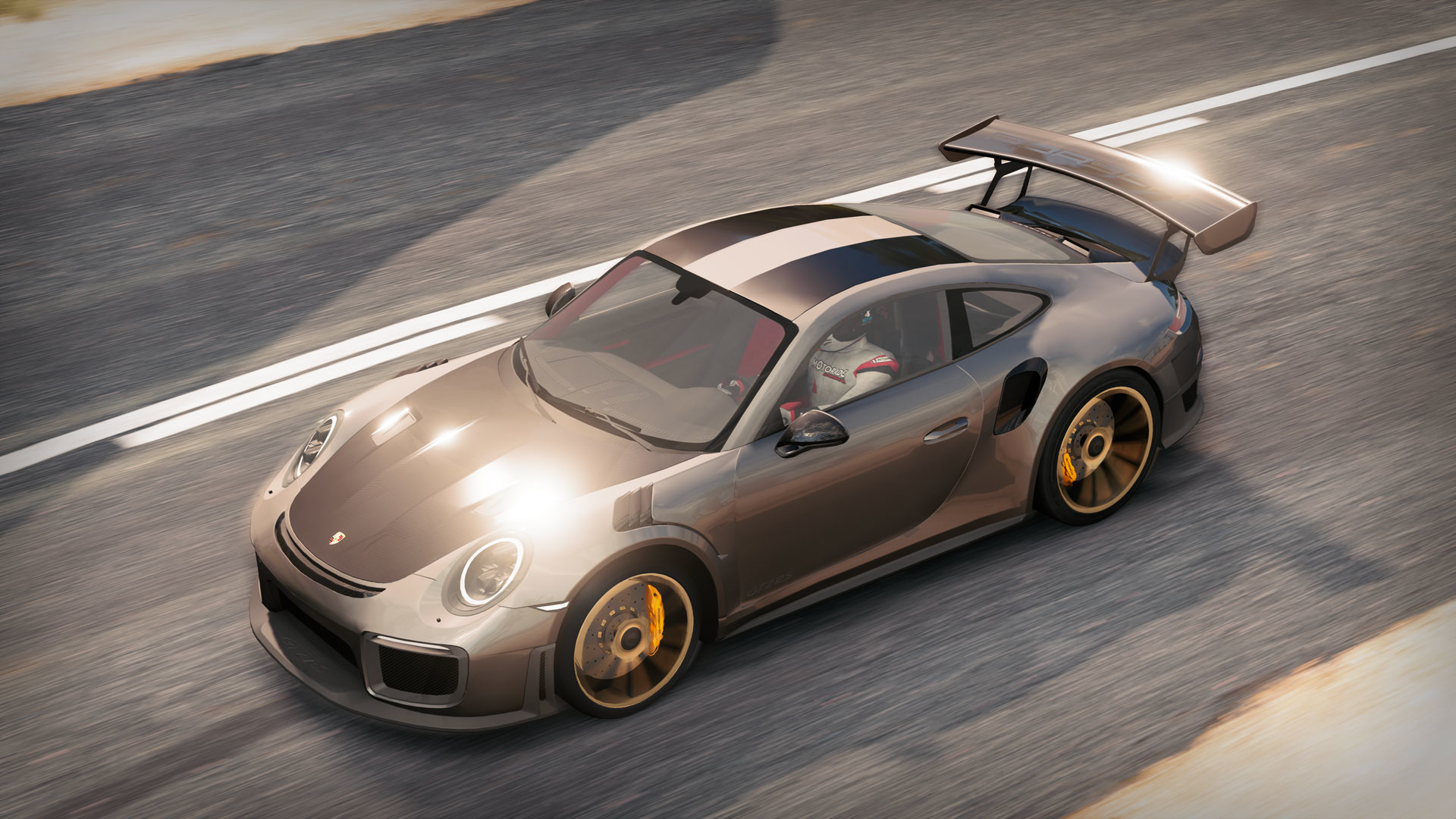 Ein grauer Porsche, der aus der Vogelperspektive auf einer Asphaltstraße fährt.