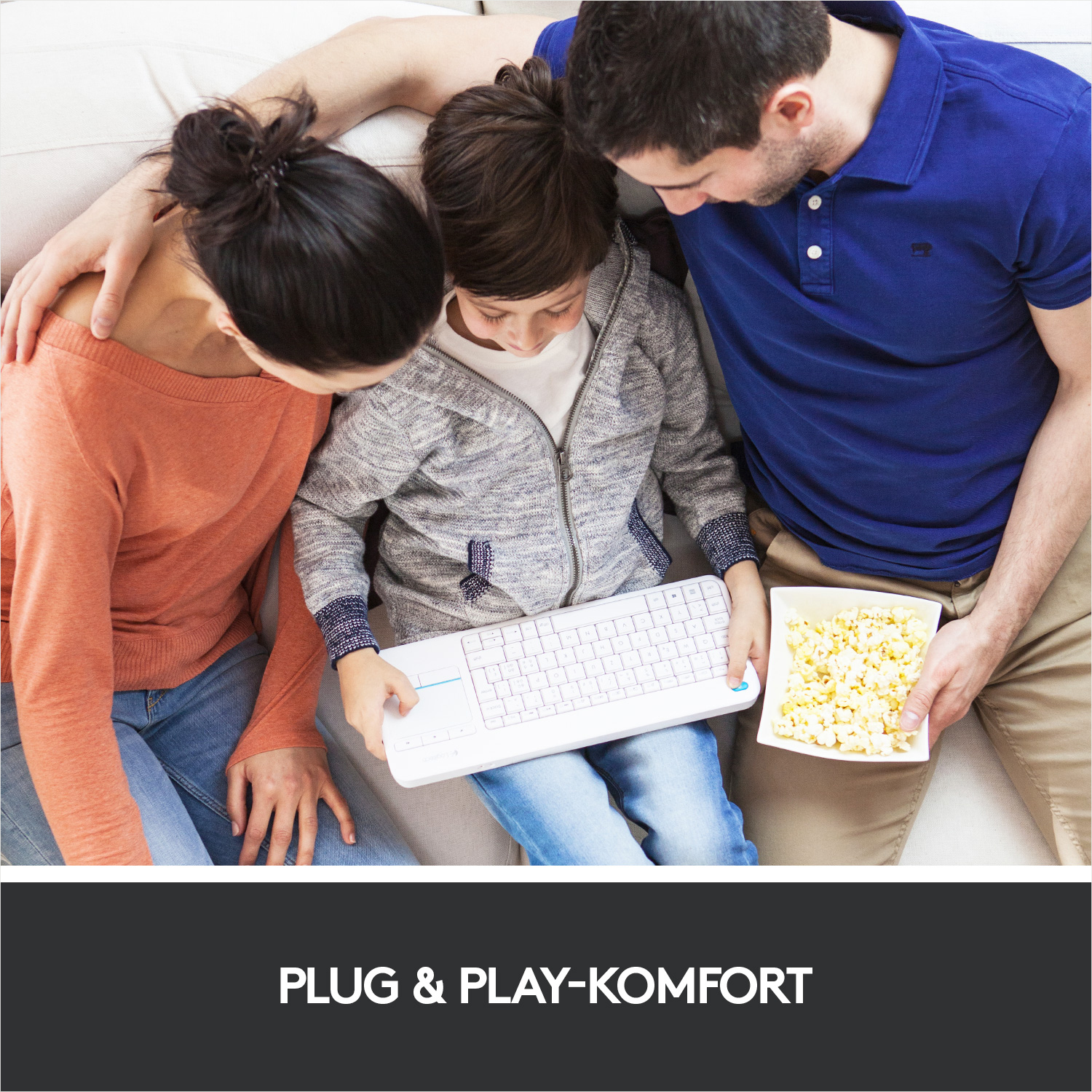 Eine dreiköpfige Familie betrachtet eine Tastatur mit Popcorn im Vordergrund. Die Familie sitzt auf einem Sofa.
