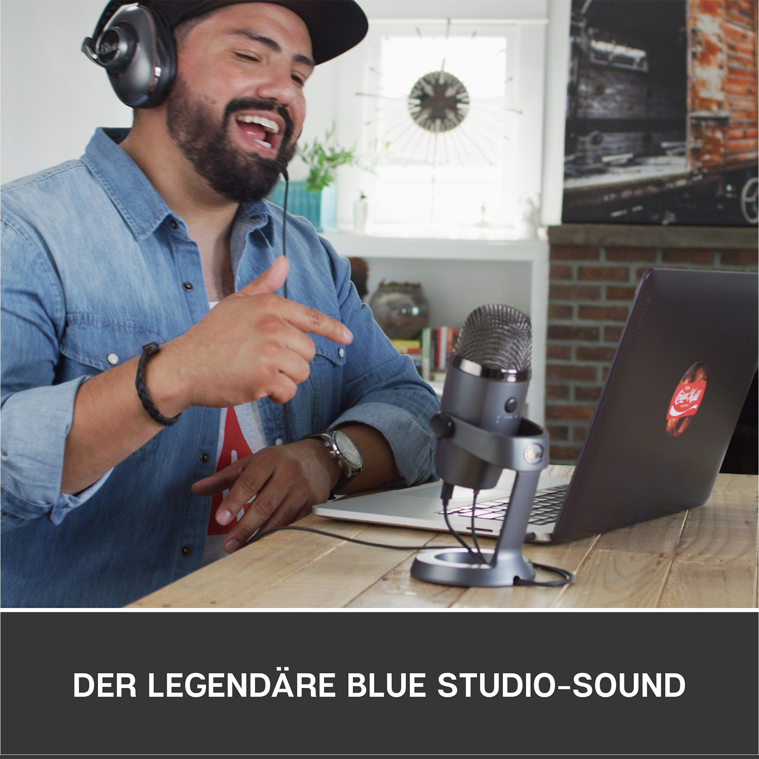 Ein Mann mit Kopfhörern singt in ein blaues Mikrofon. Ein Laptop mit Coca-Cola-Aufkleber ist sichtbar.