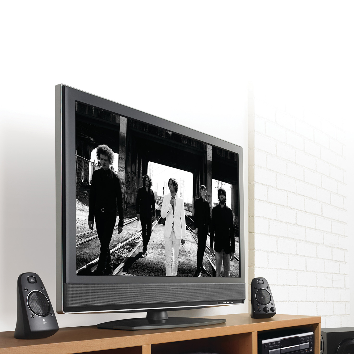Ein Fernseher mit einer Band auf dem Bildschirm. Zwei Lautsprecher stehen auf einem Holztisch.