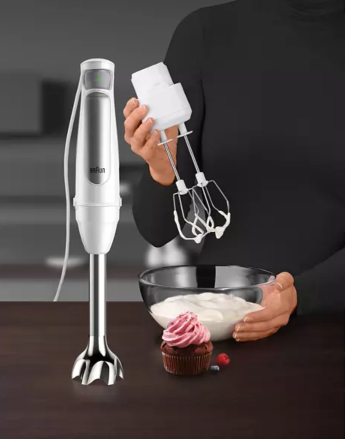 Un mixeur avec accessoires, un cupcake et un bol de crème sur une table.