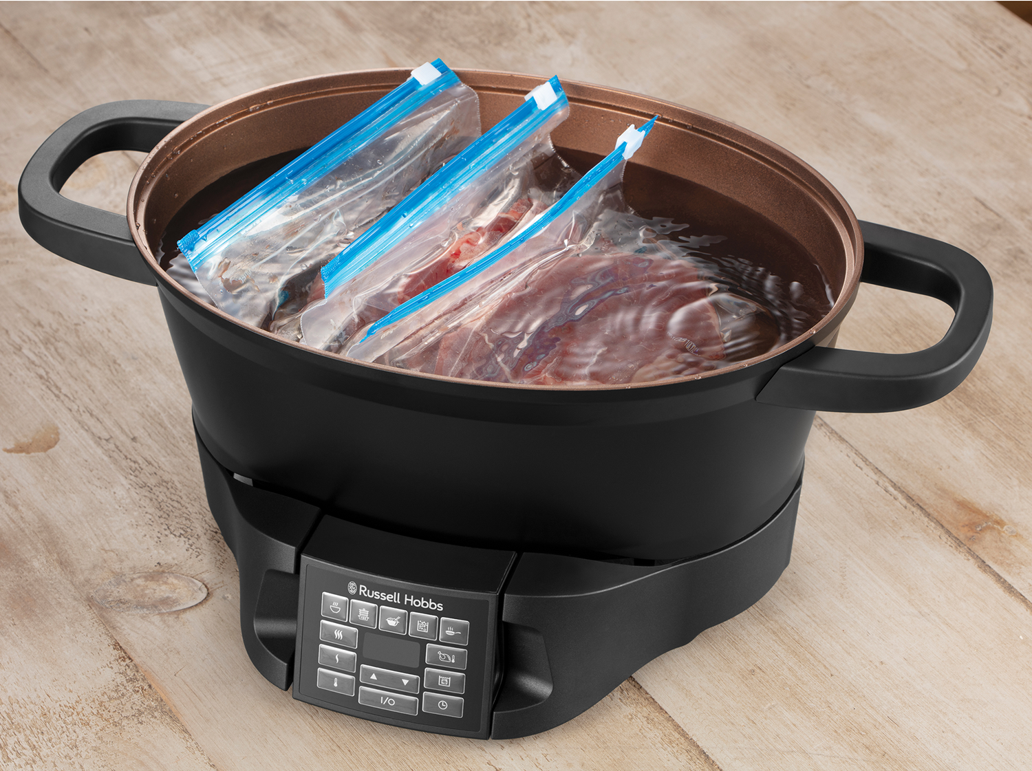 Black and copper-colored slow cooker with water and food bags inside.