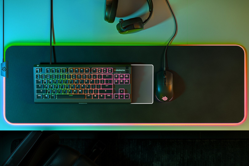 Gaming setup: black keyboard, mouse, and headset on a large, illuminated mousepad.