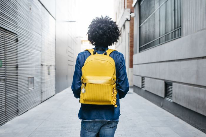 Person, die mit gelbem Rucksack in einer engen Gasse von der Kamera weggeht.
