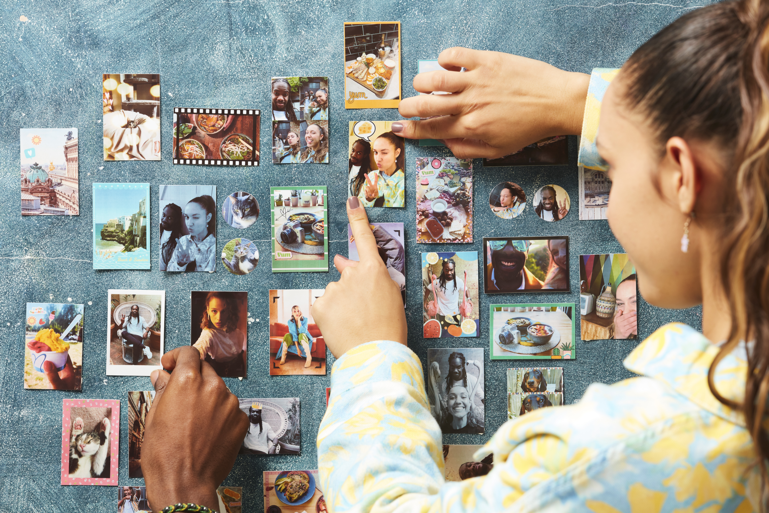Hände einer Person, die Fotos auf einer Magnettafel mit verschiedenen Bildern anordnen.