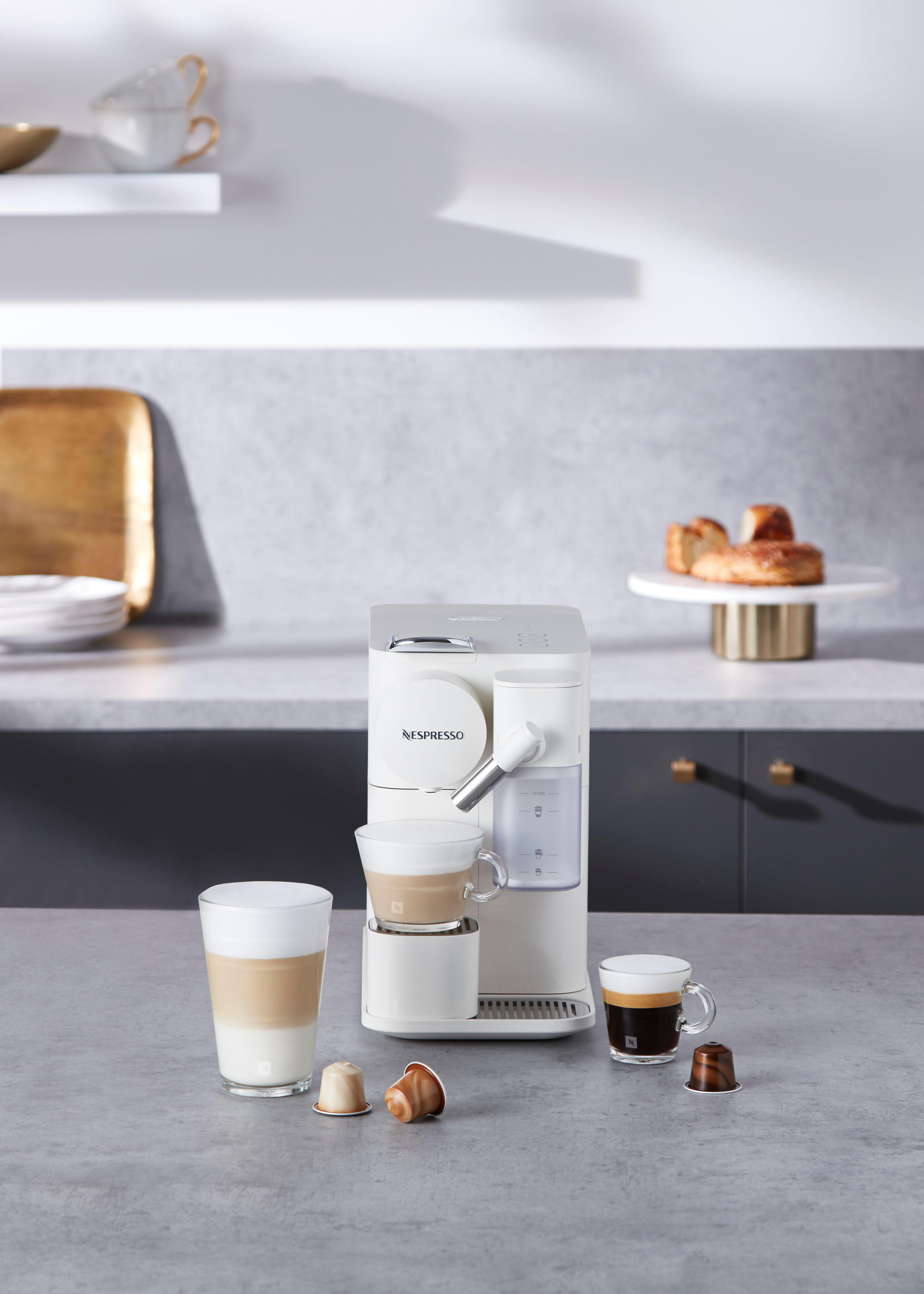 Eine weiße Nespresso-Maschine mit Kaffeetassen und Kapseln auf einer Theke.